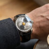 On-wrist view of the moonphase wandering hour mechanical watch with a silver dial and black leather strap